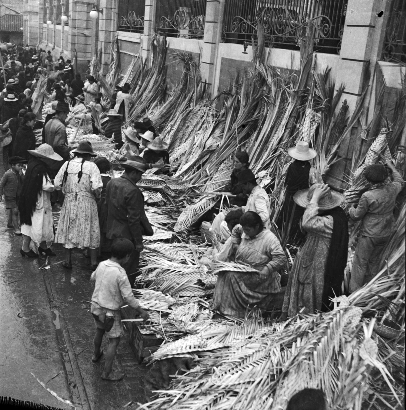 A black and white image of group of people selling fronds of palms finely interweaving