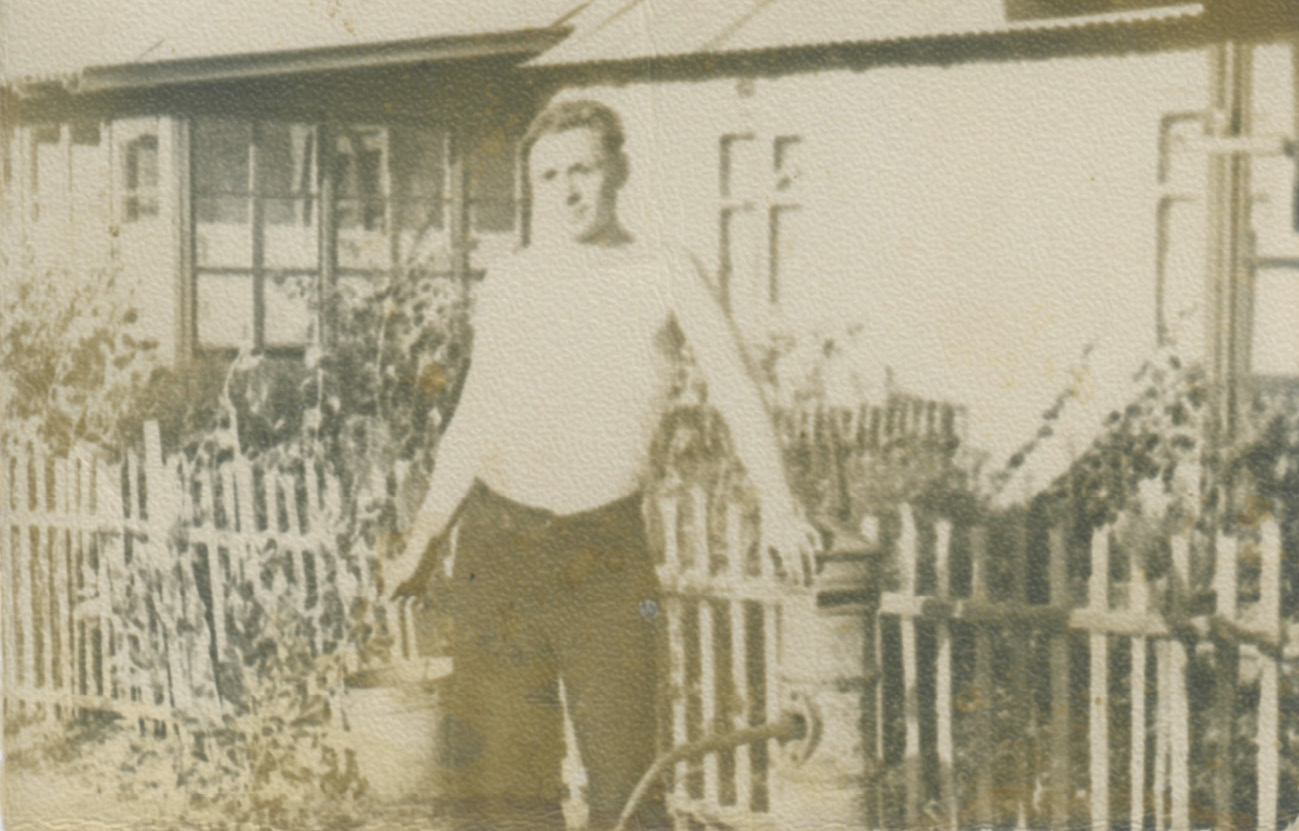 old photo of a man with a watering can in front of a house