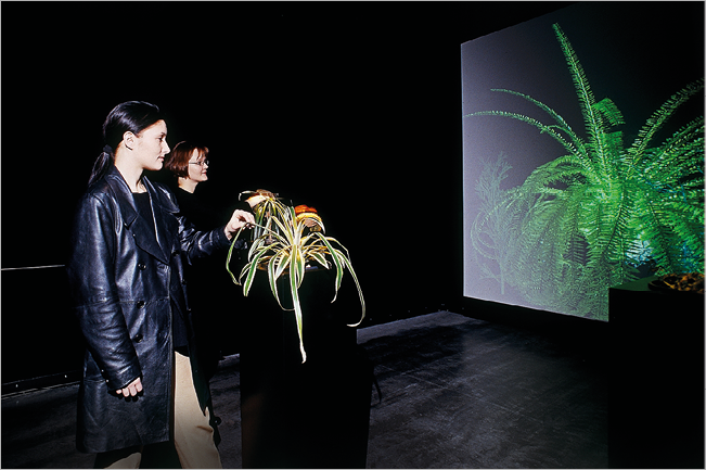 Photograph of two women and a plant in front of a screen with another plant displayed